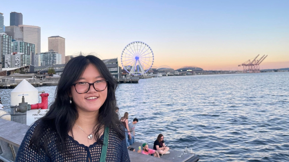 Female with glasses standing in front of the ocean. 